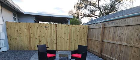 A patio with two black wicker chairs with red cushions, a small table, and a fire pit.