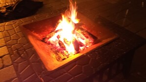 A square fire pit with flames in the center, surrounded by a stone-tiled floor.