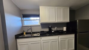 A kitchen with white cabinets, a stainless steel sink, a coffee maker, and a black refrigerator.