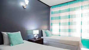 Une chambre d’hôtel avec deux lits, une table de chevet avec une lampe et une fenêtre avec des rideaux à rayures.