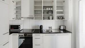 Moderni keittiö, jossa on valkoiset kaapit, musta työtaso, mikroaaltouuni, liesi, pesuallas ja kahvinkeitin.