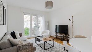 Moderni olohuone, jossa on sohva, sohvapöytä, jalustalla oleva televisio ja ruokapöytä.