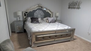 A bedroom with a bed, two bedside tables, a chair, and a wall-mounted light fixture.