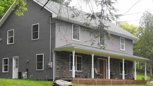 Ein zweistöckiges Haus mit Natursteinfundament, überdachter Veranda und großem Vorgarten.