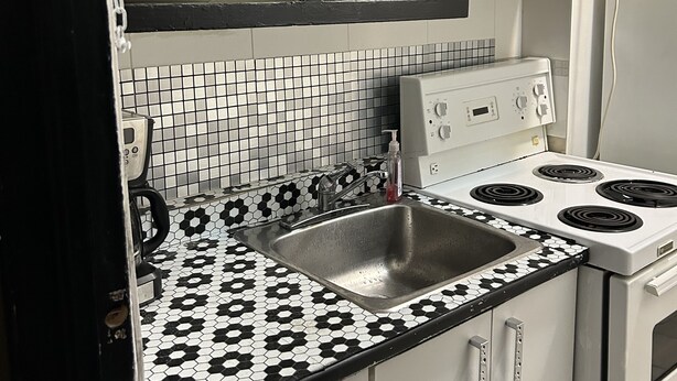 A kitchen with a black and white tiled backsplash, a stainless steel sink, a white stove with four burners, and a microwave above the stove.
