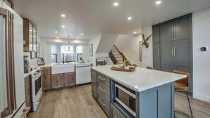 A modern kitchen with a central island, built-in appliances, and a staircase leading to an upper level.