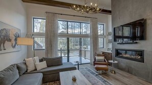 A modern living room with a large window, a fireplace, a sofa, a coffee table, and a television mounted on the wall.