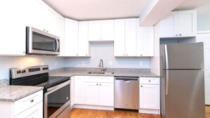 Eine moderne Küche mit weißen Schränken, einem Edelstahl-Kühlschrank, einer Mikrowelle, einem Backofen und einem Geschirrspüler.