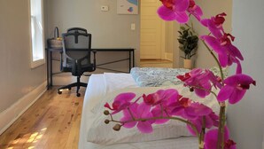 Ein Schlafzimmer mit Bett, Schreibtisch, Stuhl, Zimmerpflanze und Deckenleuchte.