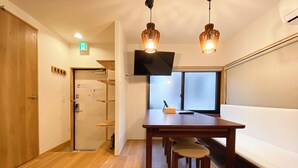 Een kamer met houten vloer, een tafel met stoelen, een aan de muur bevestigde televisie, en een raam met uitzicht.