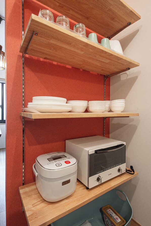 A kitchen area with a rice cooker, a toaster oven, and shelves with bowls and jars.