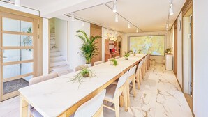 Een ruime eetruimte met een lange tafel, meerdere stoelen en potplanten.