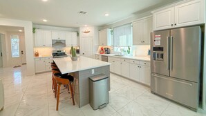 A modern kitchen with white cabinets, stainless steel appliances, and a central island with seating. - Airy Desert Getaway  (Indio)