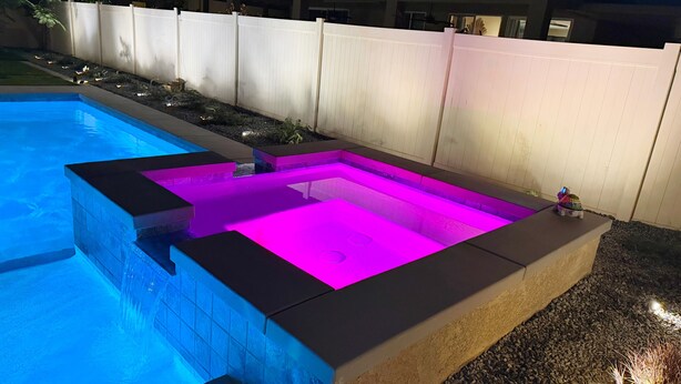 A swimming pool with a built-in hot tub area, surrounded by a white fence and a house in the background. - Airy Desert Getaway  (Indio)