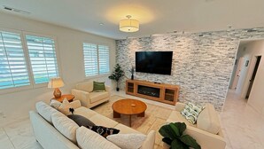 A modern living room with a stone wall, a flat-screen TV, and a sofa set. - Airy Desert Getaway  (Indio)