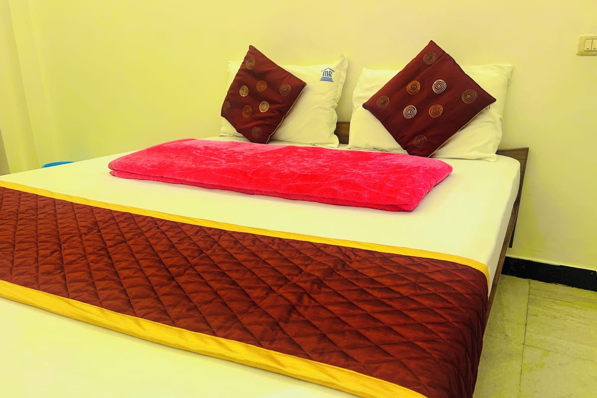 Ein Bett mit einer roten Decke, zwei Kissen mit einem Rundmuster und einer gesteppten, braunen Bettdecke.