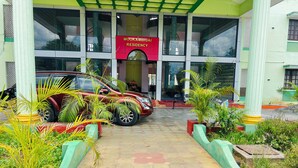 Fachada de un edificio con un coche rojo estacionado frente a él, rodeada de plantas en macetas y un camino de baldosas.