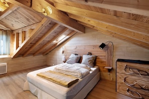 Ein Holzinnenraum mit schrägverlaufender Decke, einem Bett mit Kissen, einem Nachttisch und einer Kommode mit Geweihen.
