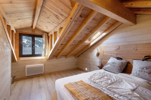 A wooden room with a sloped ceiling, a bed with white bedding, a radiator, and a window with curtains. - Village house Ramballade for 6, 300m from the slopes, in the heart of Les Angles with garage (Les Angles)