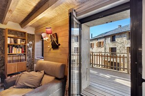 A cozy room with a wooden ceiling, a leather sofa, a bookshelf, and a view of a stone building through a glass door. - Village house Ramballade for 6, 300m from the slopes, in the heart of Les Angles with garage (Les Angles)
