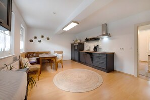 Et moderne køkken med indbygget ovn, spiseplads med bord og stole, samt et stort vindue der giver naturligt lys.