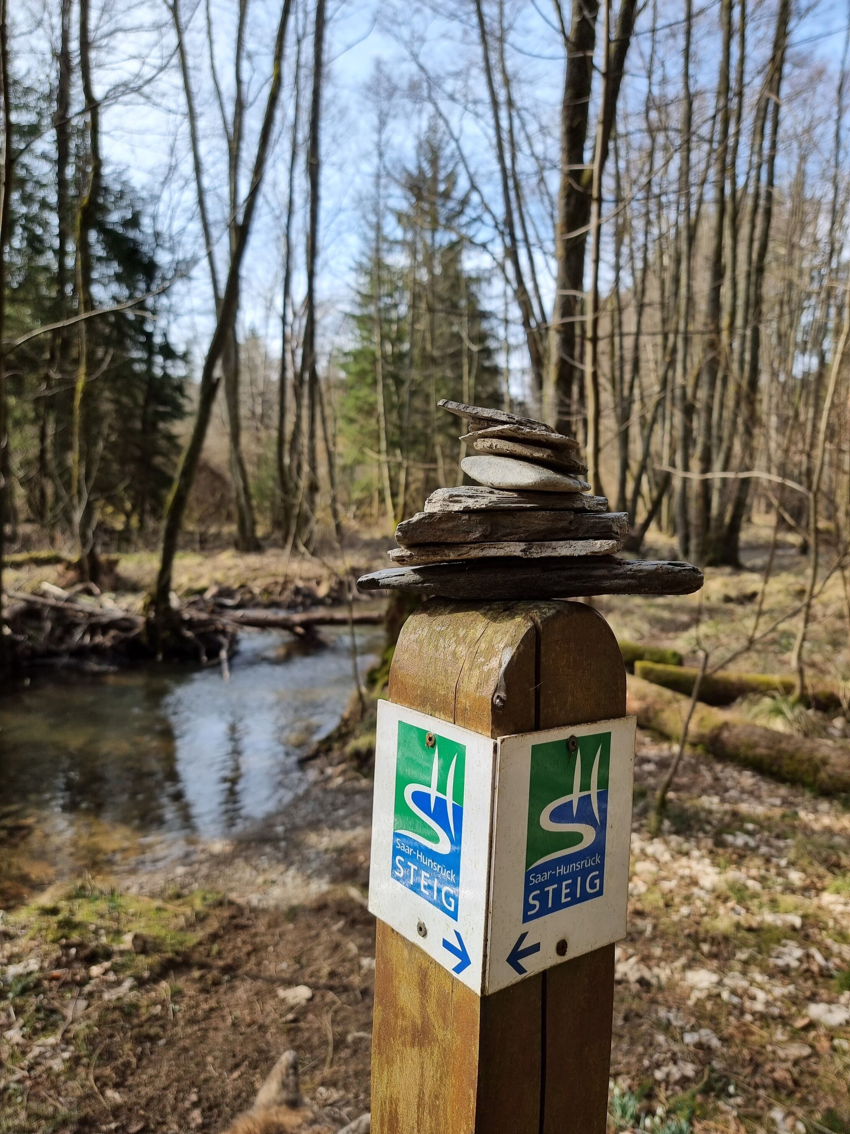 A wooden post with directional signs and a stack of stones.