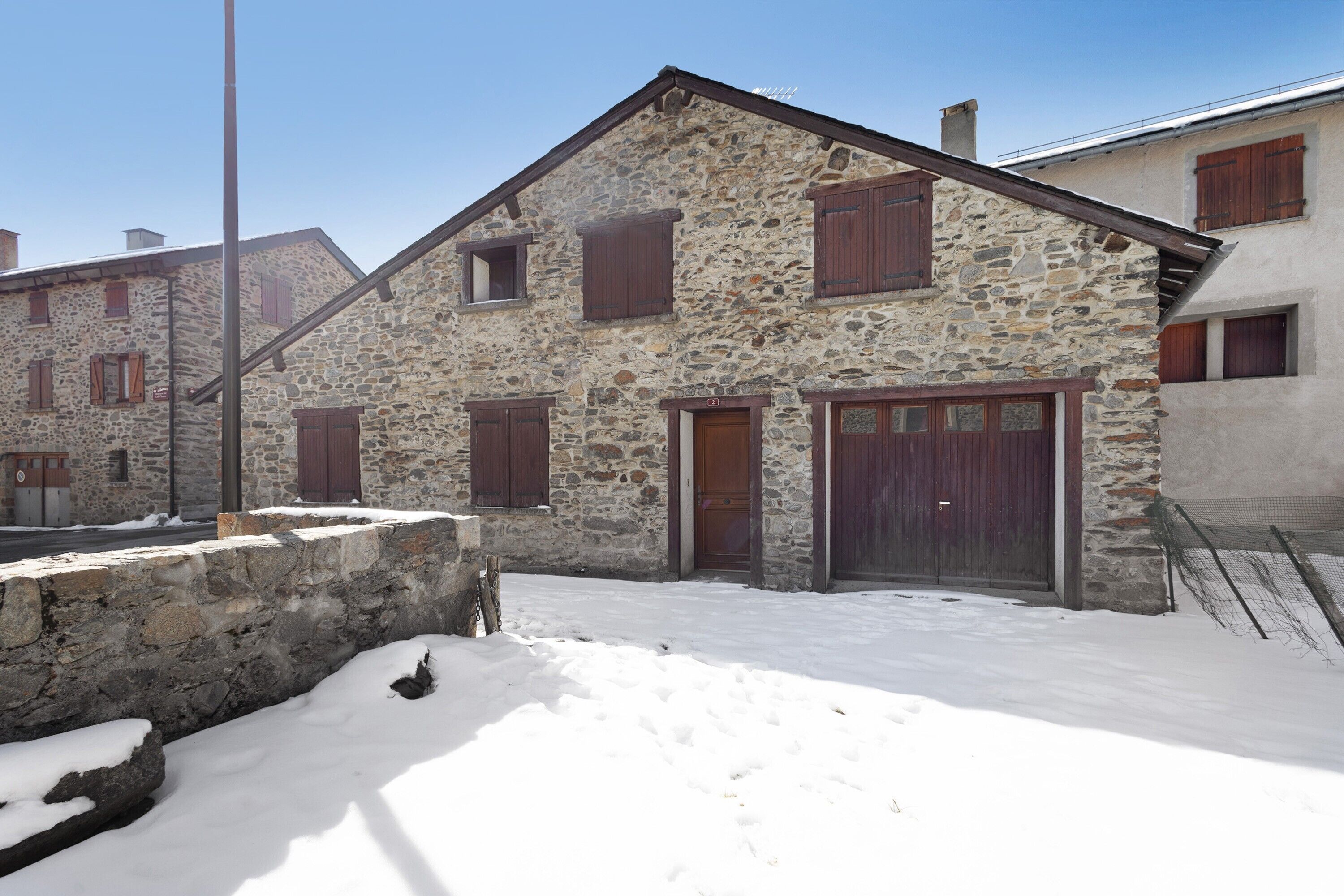 A stone building with a wooden door and windows, surrounded by snow.