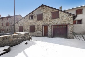 A stone building with a wooden door and windows, surrounded by snow.
