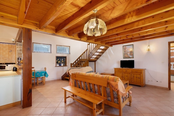 A wooden interior with a bench, a staircase, a television, and a kitchen area.