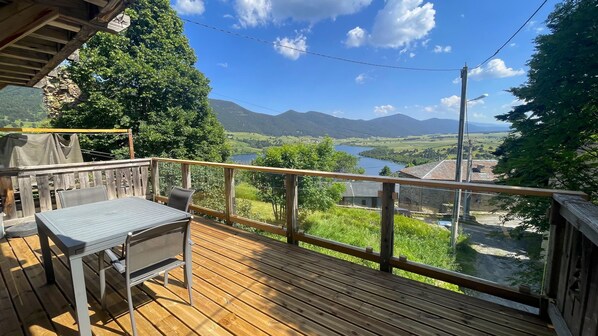 A wooden deck with a table and chairs, overlooking a scenic valley with mountains and a lake. - Village House Puyvalador: Mountain Charm, Breathtaking Views of Lake Puyvalador (Puyvalador)