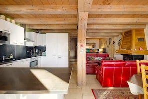 A modern kitchen with white cabinets and stainless steel appliances, a red leather sofa in a cozy living area, and a wooden ceiling.
