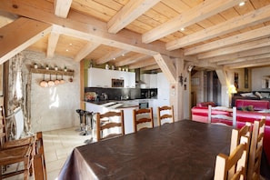 Une cuisine rustique avec des poutres en bois, un coin repas avec une grande table et des chaises, et un canapé rouge dans le salon.