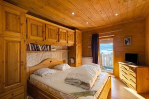 A wooden bedroom with a bed, a television, and a window with a view. - Village House Puyvalador: Mountain Charm, Breathtaking Views of Lake Puyvalador (Puyvalador)