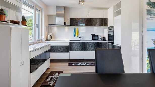 A modern kitchen with white cabinets, a black countertop, and a dining area with a table and chairs.