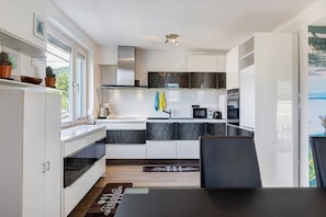 A modern kitchen with white cabinets, a black countertop, and a dining area with a table and chairs. - Apartment 'Lerchenweg B' with Shared Terrace, Shared Garden and Wi-Fi (Bad Wildungen)