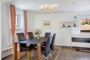 A dining area with a table, chairs, a vase of flowers, a painting, and a kitchen area with cabinets and a window. - Apartment 'Lerchenweg B' with Shared Terrace, Shared Garden and Wi-Fi (Bad Wildungen)