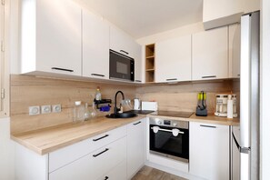 Une cuisine moderne avec des armoires blanches, un plan de travail en bois, un four à micro-ondes encastré, un four et un réfrigérateur.