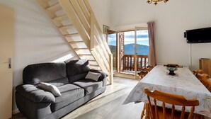 Een moderne woonkamer met een bank, eettafel, houten trap en een televisie.
