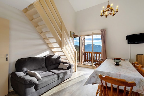 Un salon moderne avec un canapé, une table à manger, un escalier en bois et un téléviseur.