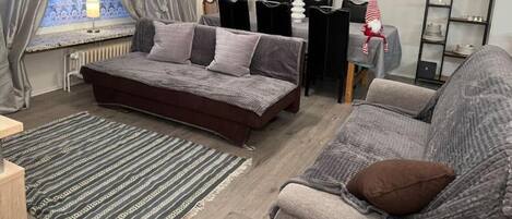A bedroom with a large bed, a sofa, a dining table, and a window with curtains.