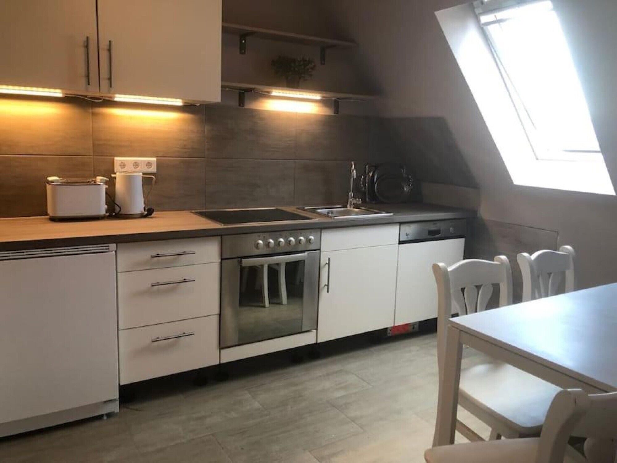 A modern kitchen with a built-in oven, a dishwasher, and a window providing natural light.