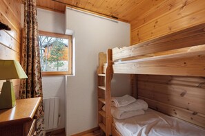Una cama litera de madera con ventana, un radiador y una lámpara sobre una mesa de madera.