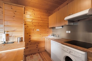 A compact kitchen with wooden walls, a stainless steel range hood, a built-in dishwasher, and a granite countertop. - Chalet le Cerf - 3 Bedrooms, South-Facing Terrace with Stunning View, 1 km from Slopes (Les Angles)