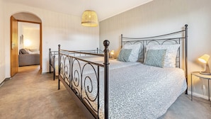 Un dormitorio con una cama, una mesita de noche con lámpara, un candelabro colgante y un arco de entrada a otra habitación.