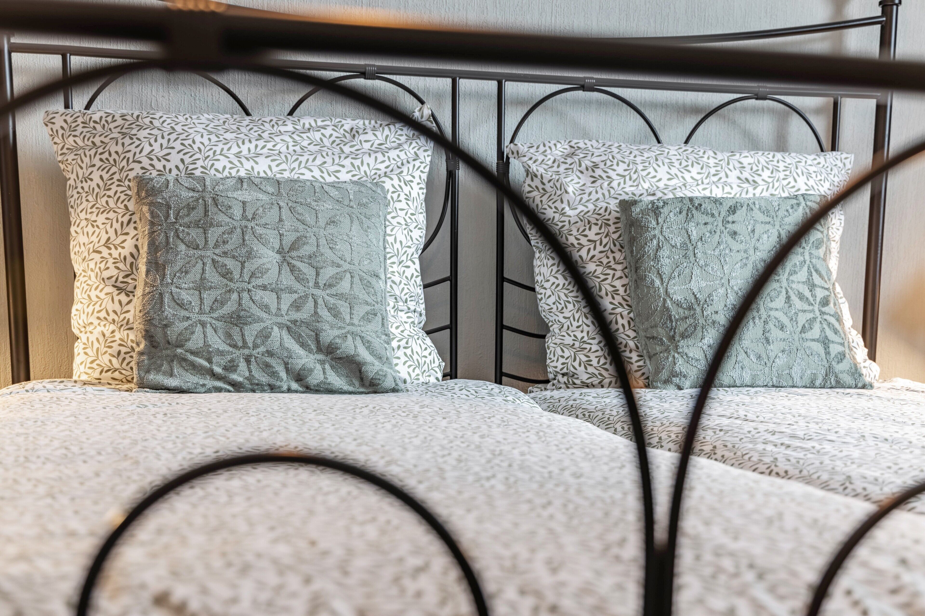 A bed with a metal frame, two patterned pillows, and a textured blanket.