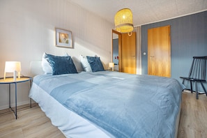 A hotel room with a large bed, a bedside table with a lamp, a framed picture on the wall, and a wooden door.