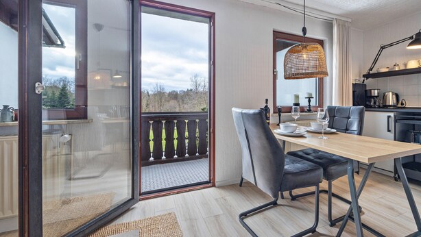 A modern kitchen with a dining area, a sliding glass door to a balcony, and a hanging light fixture. - Apartment 'Hochwald' with Shared Terrace, Shared Garden and Wi-Fi (Bad Sachsa)
