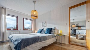 A bedroom with a bed, bedside table, lamp, and a view through an open door to a dining area. - Apartment 'Hochwald' with Shared Terrace, Shared Garden and Wi-Fi (Bad Sachsa)