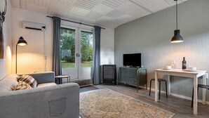 A modern living room with a sofa, a TV, a small table, and a kitchen area with a stove. - Chalet 'Hochwald' with Shared Terrace, Private Garden and Wi-Fi (Bad Sachsa)