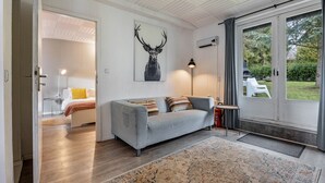 A modern living room with a grey sofa, a rug, a deer wall art, and a view of the outdoors. - Chalet 'Hochwald' with Shared Terrace, Private Garden and Wi-Fi (Bad Sachsa)
